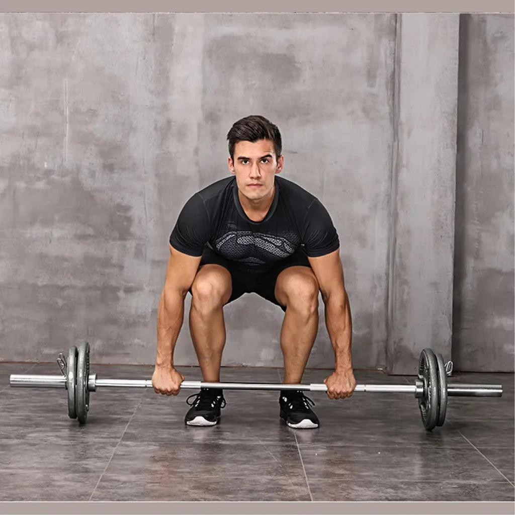 Man performing a barbell squat against a gray concrete wall.