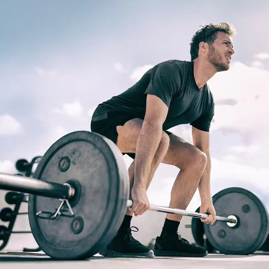 Man lifting a barbell outdoors with a clear sky background