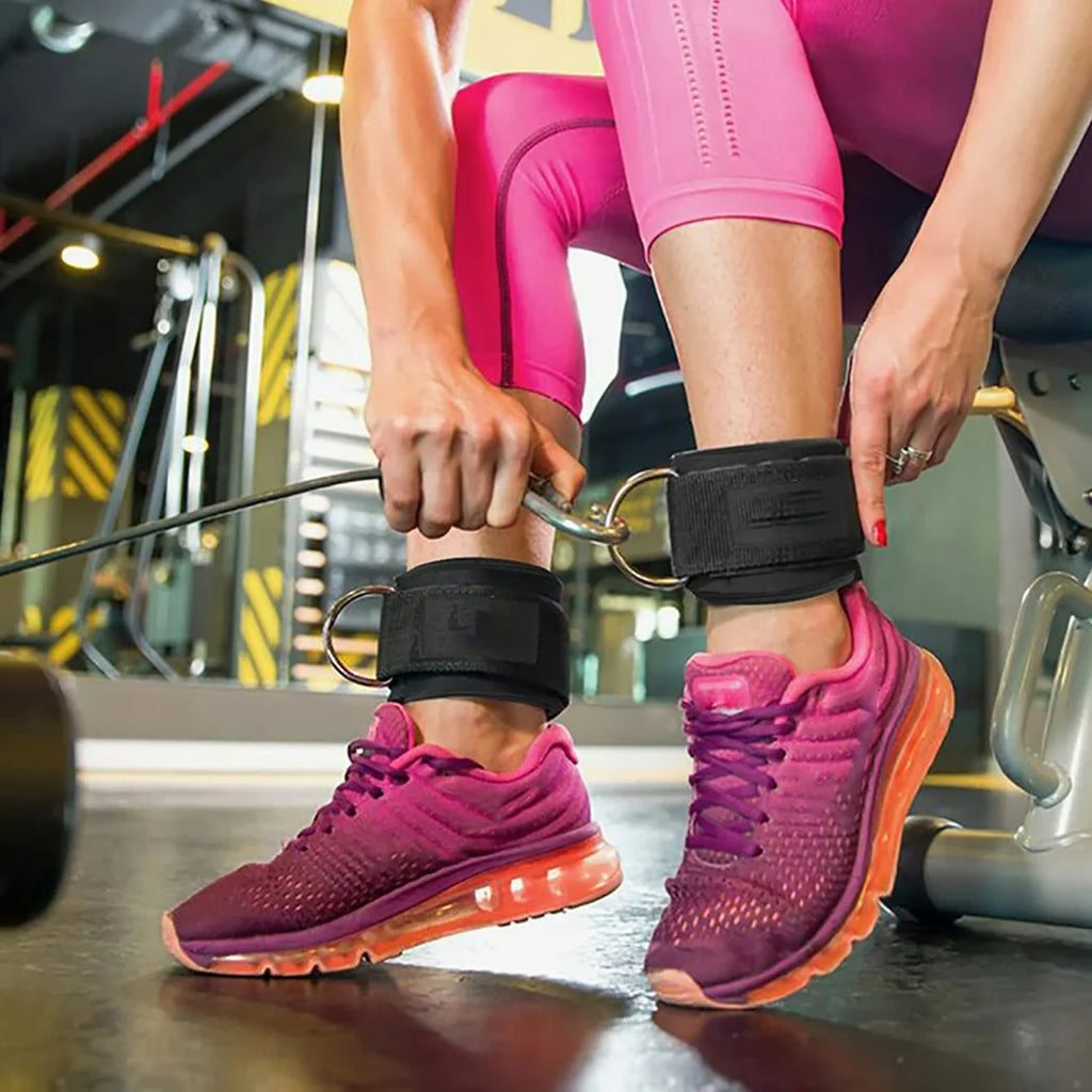 Person wearing pink athletic shoes and leggings with black ankle straps in a gym setting