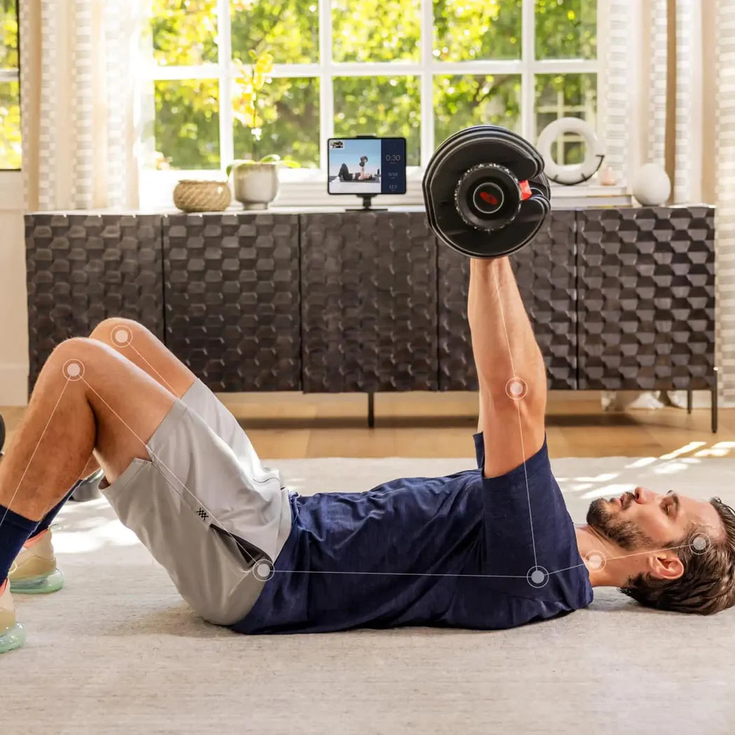 Man exercising with dumbbells in a living room setting, using a smartphone for guidance.