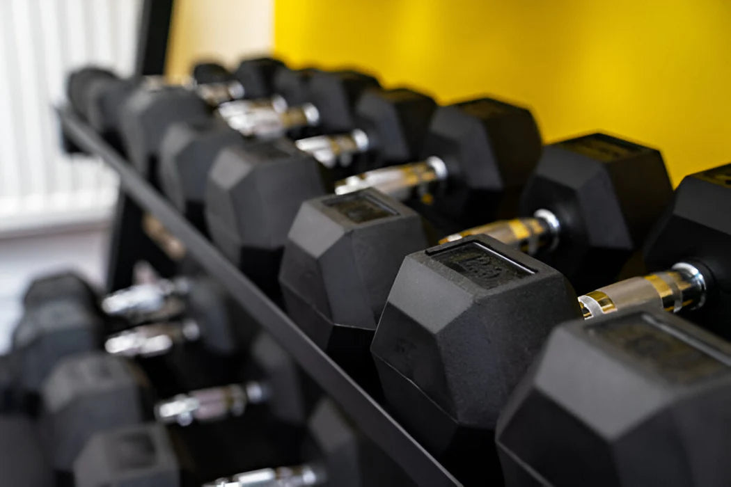 Row of black dumbbells on a rack with a yellow wall in the background