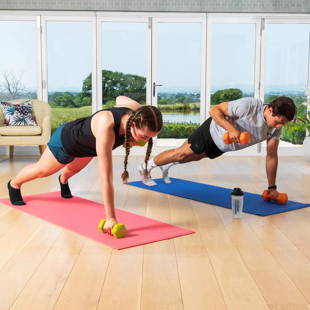 Two people exercising with dumbbells on yoga mats in a bright room with large windows.