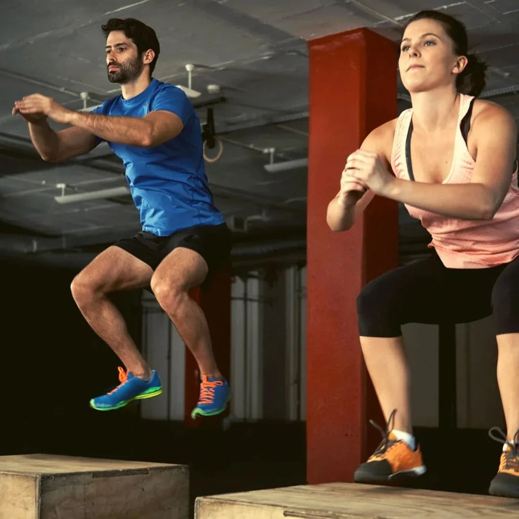 Man and woman performing box jumps in a gym setting