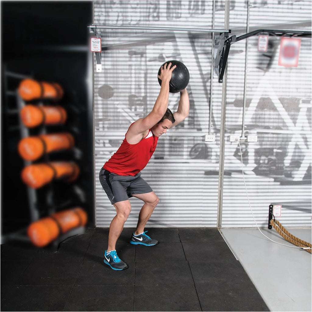 Person lifting a medicine ball in a gym setting with equipment in the background