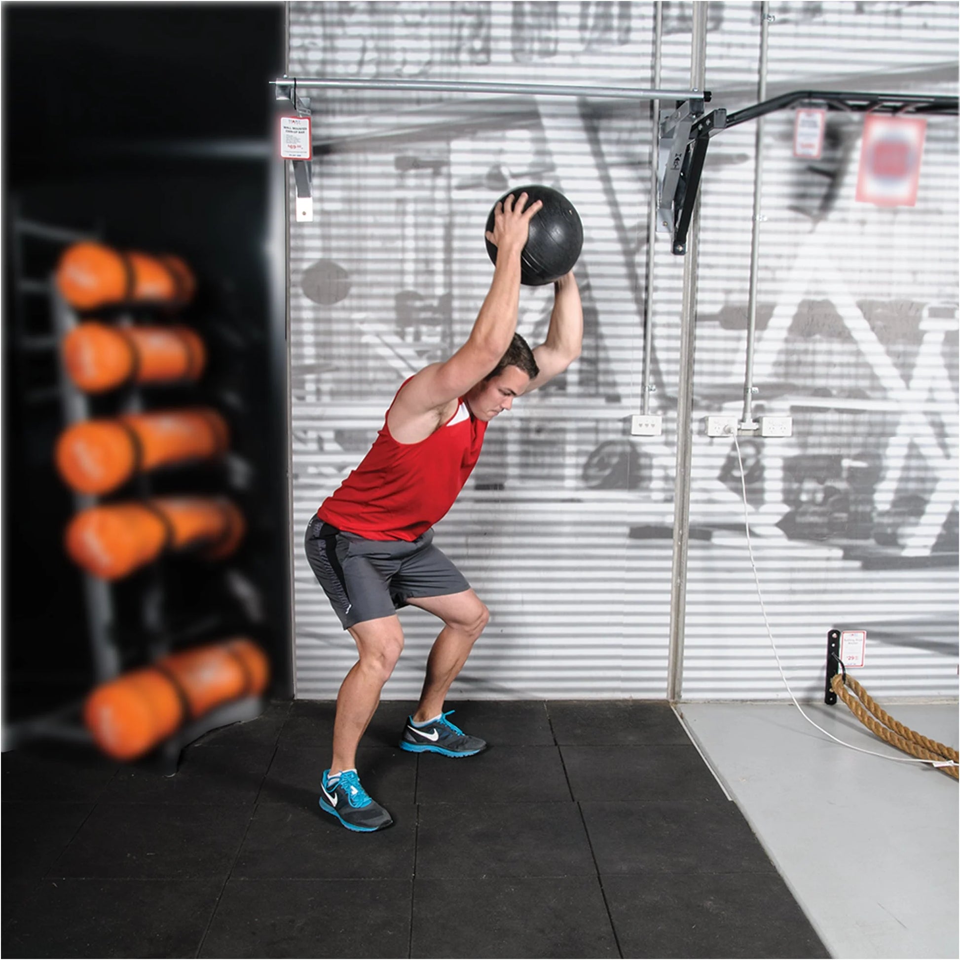 Person lifting a medicine ball in a gym setting with equipment in the background