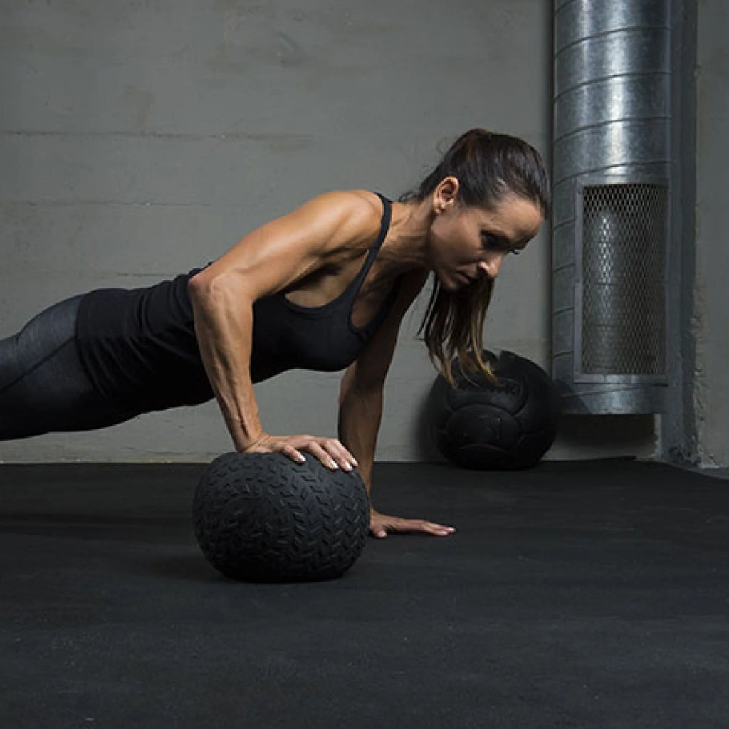 Woman performing push-ups on a black exercise ball in a gym setting.