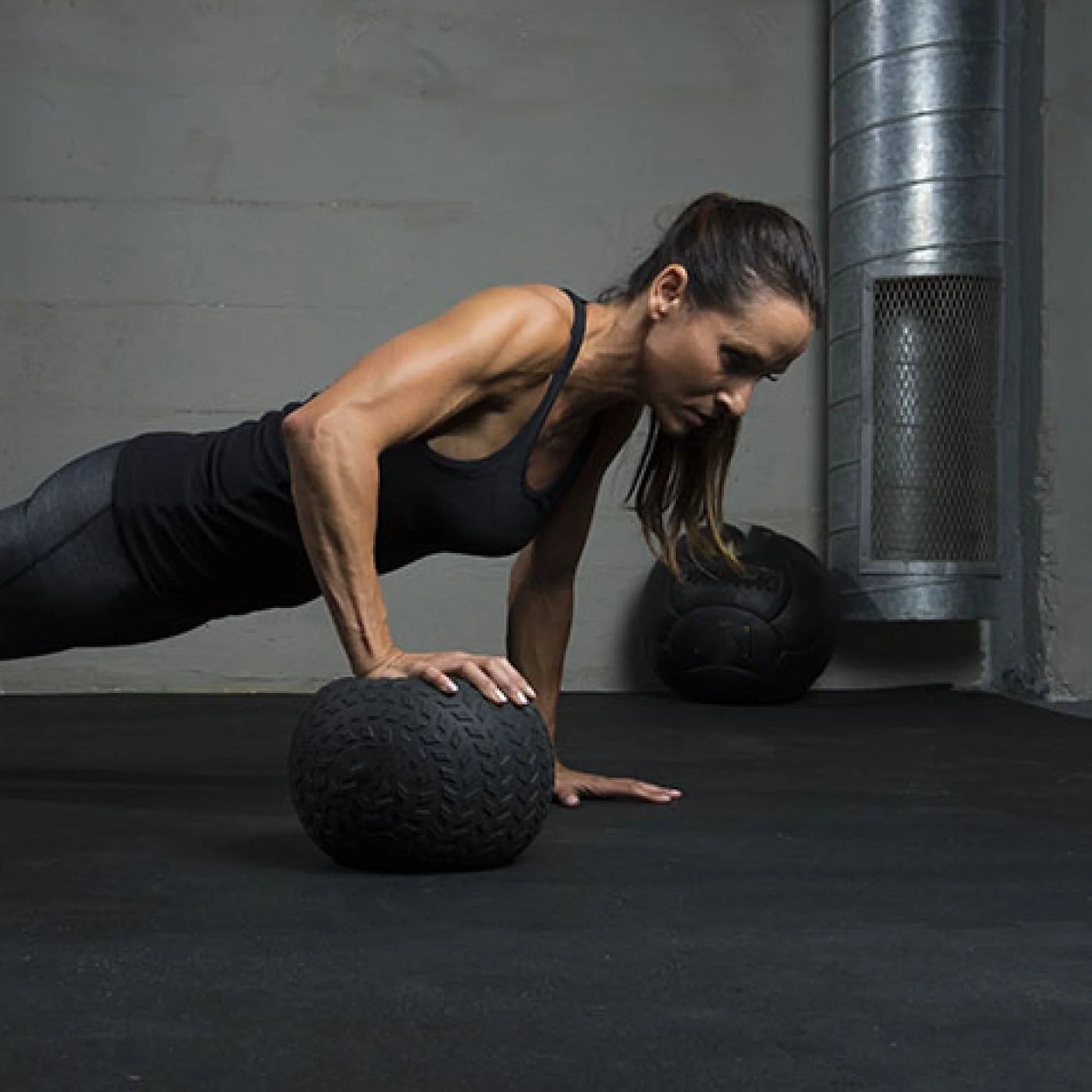Woman performing push-ups on a black exercise ball in a gym setting.