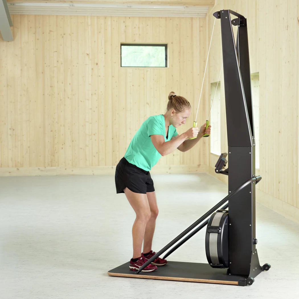 Woman using a rowing machine in a wooden-floored room.
