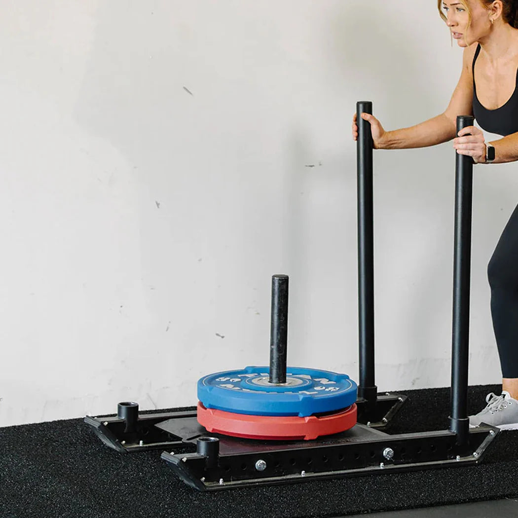 Person using a weightlifting platform with blue and red weights on a white wall background