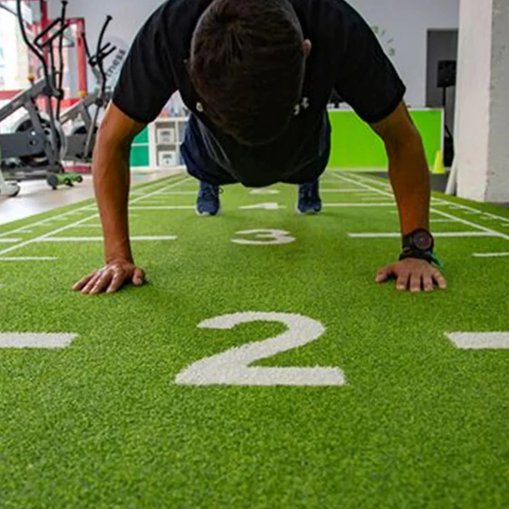 Person doing push-ups on a green turf surface with numbers