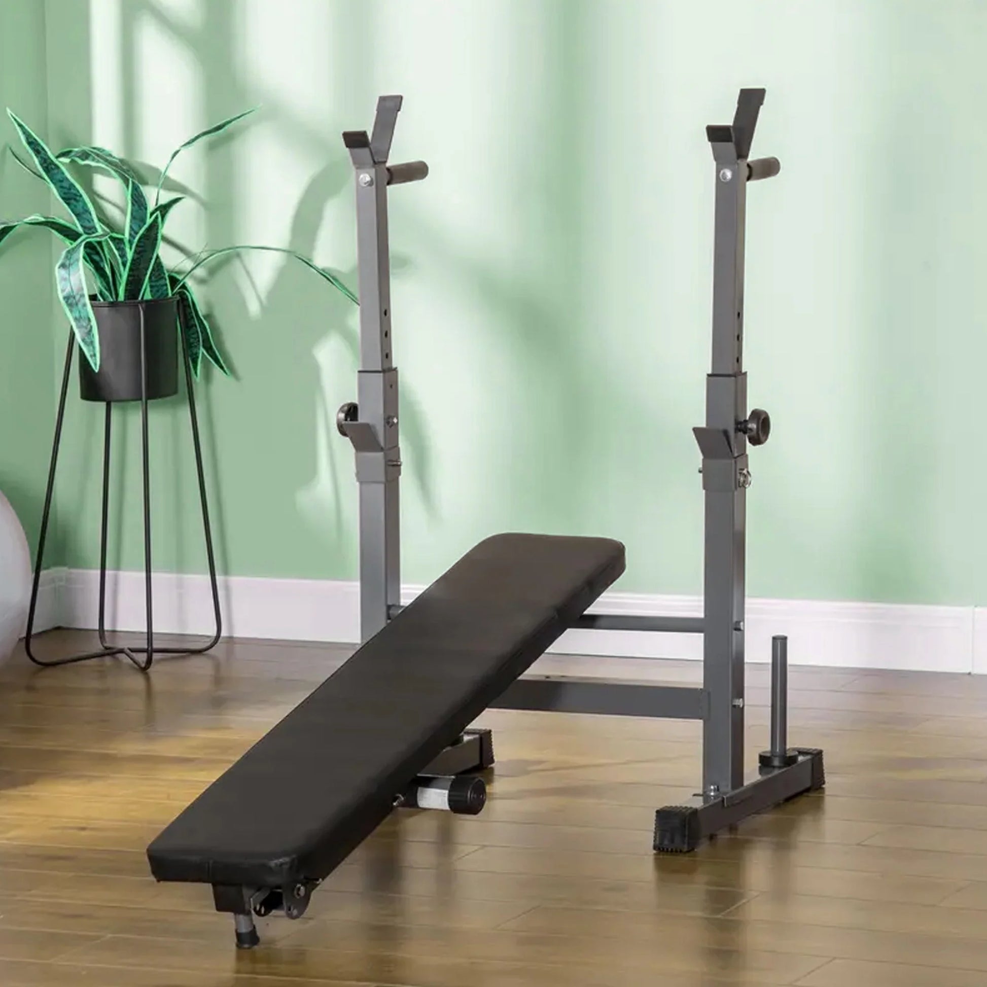 Black weight bench with adjustable stands on a wooden floor against a green wall.
